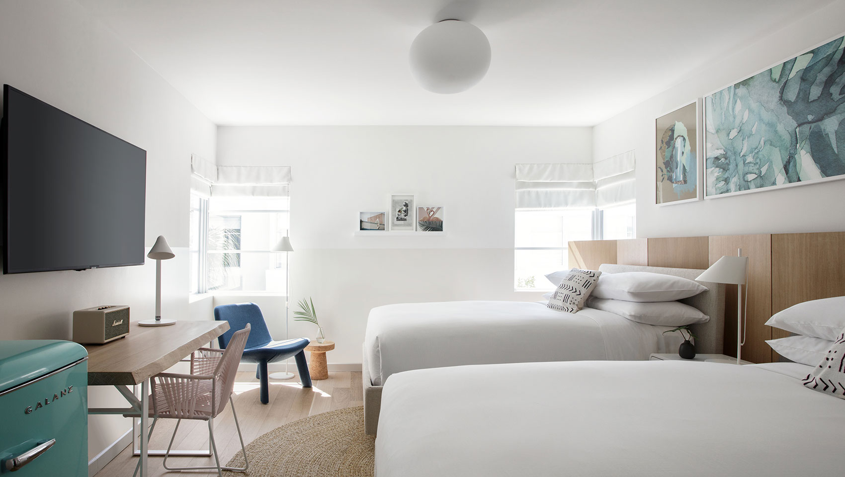 two queen beds in a guestroom with two windows and a desk